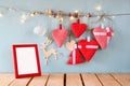 Christmas image of fabric red hearts and blank frame, garland lights, hanging on rope in front of blue wooden background Royalty Free Stock Photo