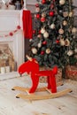 Christmas interior of living room with wooden elk rocking chair, Christmas tree, fireplace and gifts. Scandinavian wooden toy. Red Royalty Free Stock Photo