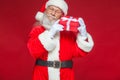 Christmas. Kind Santa Claus in white gloves holds a gift red box with a bow near an ear. He listens. Isolated on red Royalty Free Stock Photo