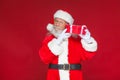 Christmas. Kind Santa Claus in white gloves holds a gift red box with a bow near an ear. He listens. on red Royalty Free Stock Photo