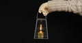 A Christmas lamp with a burning candle inside is held by the handle by a female hand in a pullover and winter parquet On Royalty Free Stock Photo