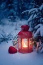 Christmas lantern under the tree with a gift in the woods. Christmas eve in the woods. Christmas lantern and toy heart in the snow Royalty Free Stock Photo