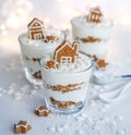 Christmas layered cream and gingerbread dessert decorated with gingerbread houses in glasses on white table