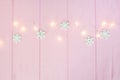 Christmas lights garland with snowflakes border over pink wooden background. Scandinavian flat lay, copy space Royalty Free Stock Photo