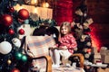 Christmas little girl with book in her hands sitting by the Christmas tree. Happy cute child in Santa hat with present Royalty Free Stock Photo