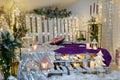Christmas living room interior with sofa made of pallets, shiny stars, garland lights, purple plaid, fir branches and candles.