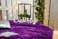 Christmas living room interior with sofa made of pallets, shiny stars, garland lights, purple plaid, fir branches and candles.