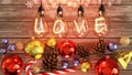 Christmas Love - cozy wooden table with xmas ornaments with cones, candy cane, shiny balls and warm incandescent bulb lights above