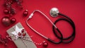 Christmas medical banner. Close up gift box, berries, red balloons and stethoscope on red background, top view, flat lay, copy Royalty Free Stock Photo