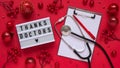 Christmas medical banner,letter board with text thanks doctors,red balls,berries,stars and stethoscope on red background top view,