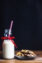 Christmas milk and chocolate cookies on wooden table over black