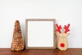 Christmas mock up with wood frame and rustic tree and wooden reindeer decor on a wood shelf against a white wall