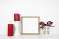 Christmas mock up with wooden frame, lantern and red candles on a white shelf against a white wall Royalty Free Stock Photo