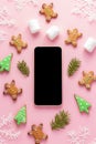 Christmas mockup of smartphone surrounded by gingerbread and marshmallows on pink background
