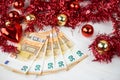 Christmas money business concept: some fifty euro banknotes with red and gold baubles and wreath decoration on light wooden table