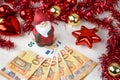 Christmas money business concept: a statuette of Santa Claus on some fifty euro banknotes with red and gold baubles and wreath