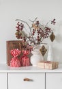 Christmas mood. Gifts, cranberry branches in a vase with paper toys on the dresser