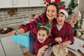 Christmas mood at home kitchen. Beautiful mom and her adorable children- boy and girl smiling toothy smile looking at web camera Royalty Free Stock Photo