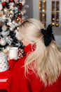 Christmas morning with blonde woman hold cup of hot coffee looking at decorated Xmas tree at home Royalty Free Stock Photo