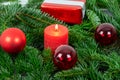Christmas motif with red burning candle surrounded by Nordmann fir branches, red christmas tree balls and gift parcel Royalty Free Stock Photo