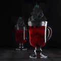 Christmas mulled wine - hot red berries tea with Christmas tree shape steam in two glass wine glasses with ripe berry in dark. Royalty Free Stock Photo