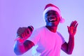 Christmas music. Cool black guy in Santa hat singing holiday song, using microphone, performing karaoke in neon light Royalty Free Stock Photo