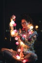 Happy woman wearing glowing jacket with sequins is holding light balls in her hands