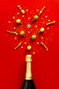 Christmas and New Year background. Champagne bottle, golden christmas balls, festive ribbons, fir branches, star confetti on red Royalty Free Stock Photo