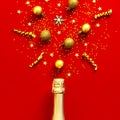 Christmas and New Year background. Champagne bottle, golden christmas balls, festive ribbons, fir branches, star confetti on red Royalty Free Stock Photo