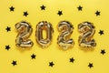 Christmas or New Year background. Text 2022, made of golden balloons, on a yellow background, with black confetti stars. Postcard Royalty Free Stock Photo