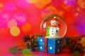 Christmas and new year card with snow globe snowman inside. Gift box on red bokeh background. Holidays, winter and celebration con Royalty Free Stock Photo