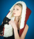Christmas and New Year celebration. Blonde woman in fur hat with little puppy. Beautiful girl in little black dress with Royalty Free Stock Photo