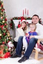 Christmas or New year celebration. Happy young family sitting in chair near Christmas tree with xmas gifts. A fireplace with chris Royalty Free Stock Photo