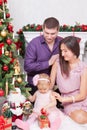 Christmas or New year celebration. Happy young family sitting in chair near Christmas tree with xmas gifts. A fireplace with chris Royalty Free Stock Photo