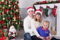 Christmas or New year celebration. Happy young family sitting near Christmas tree with xmas gifts. A fireplace with christmas stoc Royalty Free Stock Photo