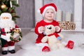 Christmas or New year celebration. Little girl in red dress and santa hat with bear toy sitting on the floor near the Christmas tr Royalty Free Stock Photo