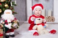 Christmas or New year celebration. Little girl in red dress and santa hat with bear toy sitting on the floor near the Christmas tr Royalty Free Stock Photo