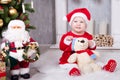 Christmas or New year celebration. Little girl in red dress and santa hat with bear toy sitting on the floor near the Christmas tr Royalty Free Stock Photo