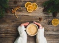 Christmas or new year composition of female hands, hot winter drink, spruce branches, orange chips, cinnamon, cones