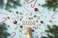 Christmas and New Year card with champagne bottle, 2024 numbers, fir tree, confetti stars and decorations top view. Flat lay style