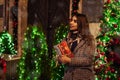 Christmas, New Year concept. Woman waiting for friends on city street by decorated cafes holding gift box. Holiday Royalty Free Stock Photo