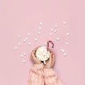 Christmas New Year drink, white mug with marshmallows in female hands in knitted sweater and Candy Cane on pink background top