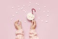 Christmas New Year drink, white mug with marshmallows in female hands in knitted sweater and Candy Cane on pink background top