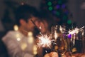 Christmas and New year party concept. Couple in love burning sparklers by illuminated Christmas tree with champagne Royalty Free Stock Photo
