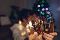 Christmas and New year party concept. Couple in love burning sparklers by illuminated Christmas tree with champagne Royalty Free Stock Photo