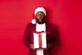 Christmas, New Year and shopping concept. Surprised african american man in santa hat saying wow, holding holiday gift