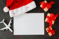 Christmas or New Year travel concept. Blank paper, toy airplane on Santa hat and gift boxes.