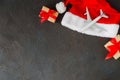 Christmas or New Year travel concept. Toy airplane on Santa hat and gift boxes on dark concrete.