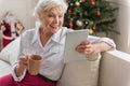 Positive old woman is relaxing on sofa with modern device Royalty Free Stock Photo