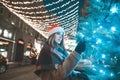 Christmas night portrait of a girl near a Christmas tree on the background of a street decorated with a garland, looks at the Royalty Free Stock Photo